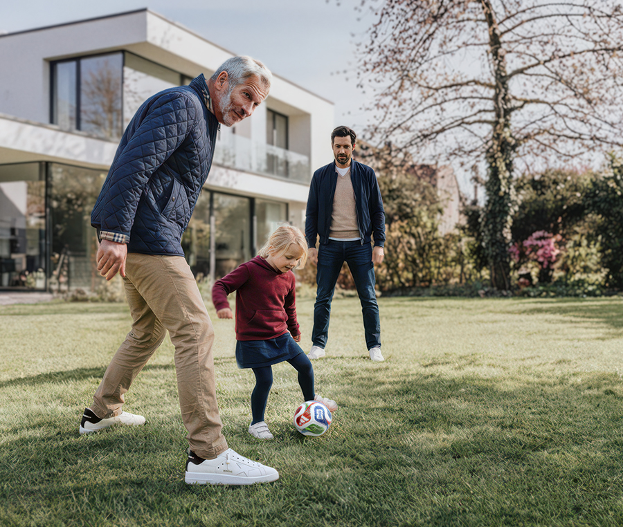 Mädchen spielt mit Opa und Vater im Garten Fußball